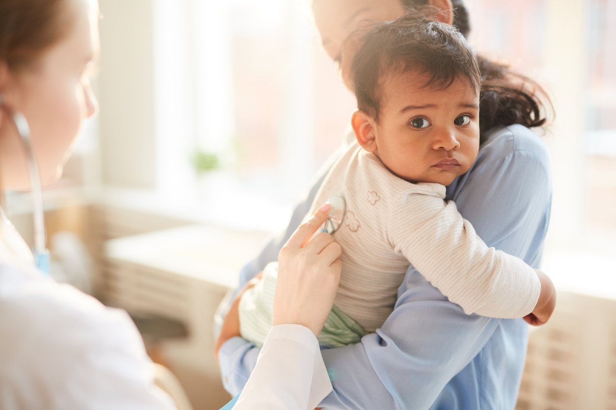 Doctor examining the child Mother holding her baby to her chest while female doctor examining him with stethoscope at hospital